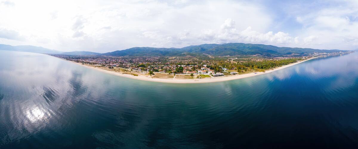 An aerial view of a coastal town with a beach, mountains in the background, and calm waters.