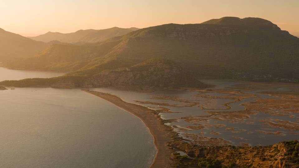 A coastal landscape with a large body of water, a sandy beach, and a mountainous backdrop.