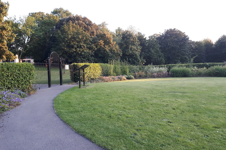 Ein Weg, der zu einem Park mit einer Rasenfläche und einem Metallgitter führt.