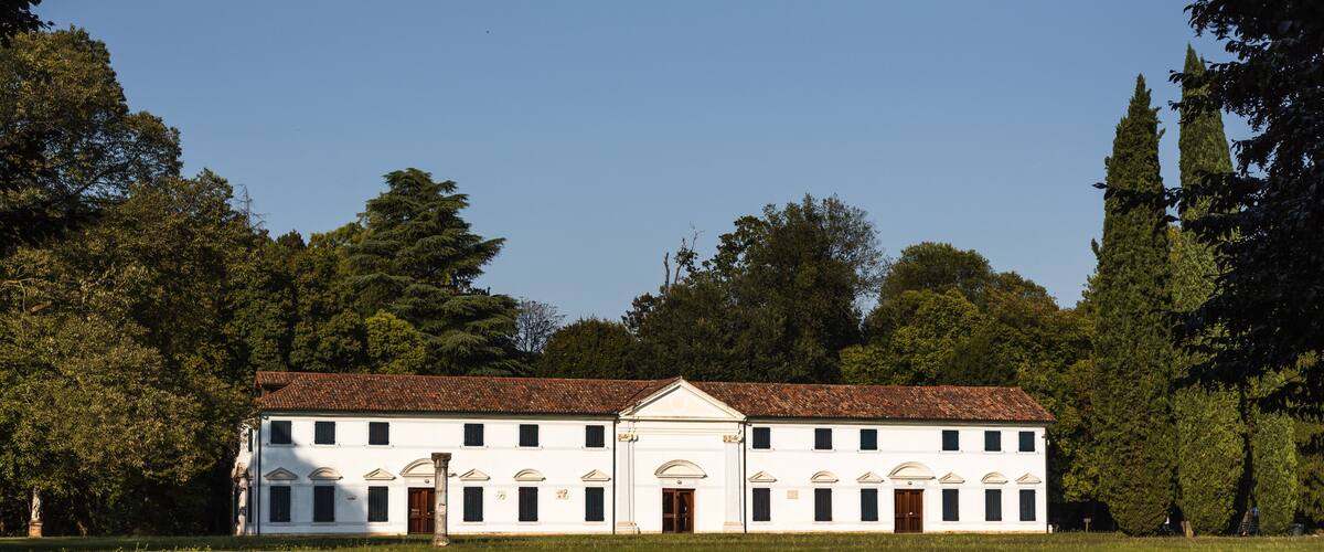 A white building with a red-tiled roof, surrounded by trees and grass.