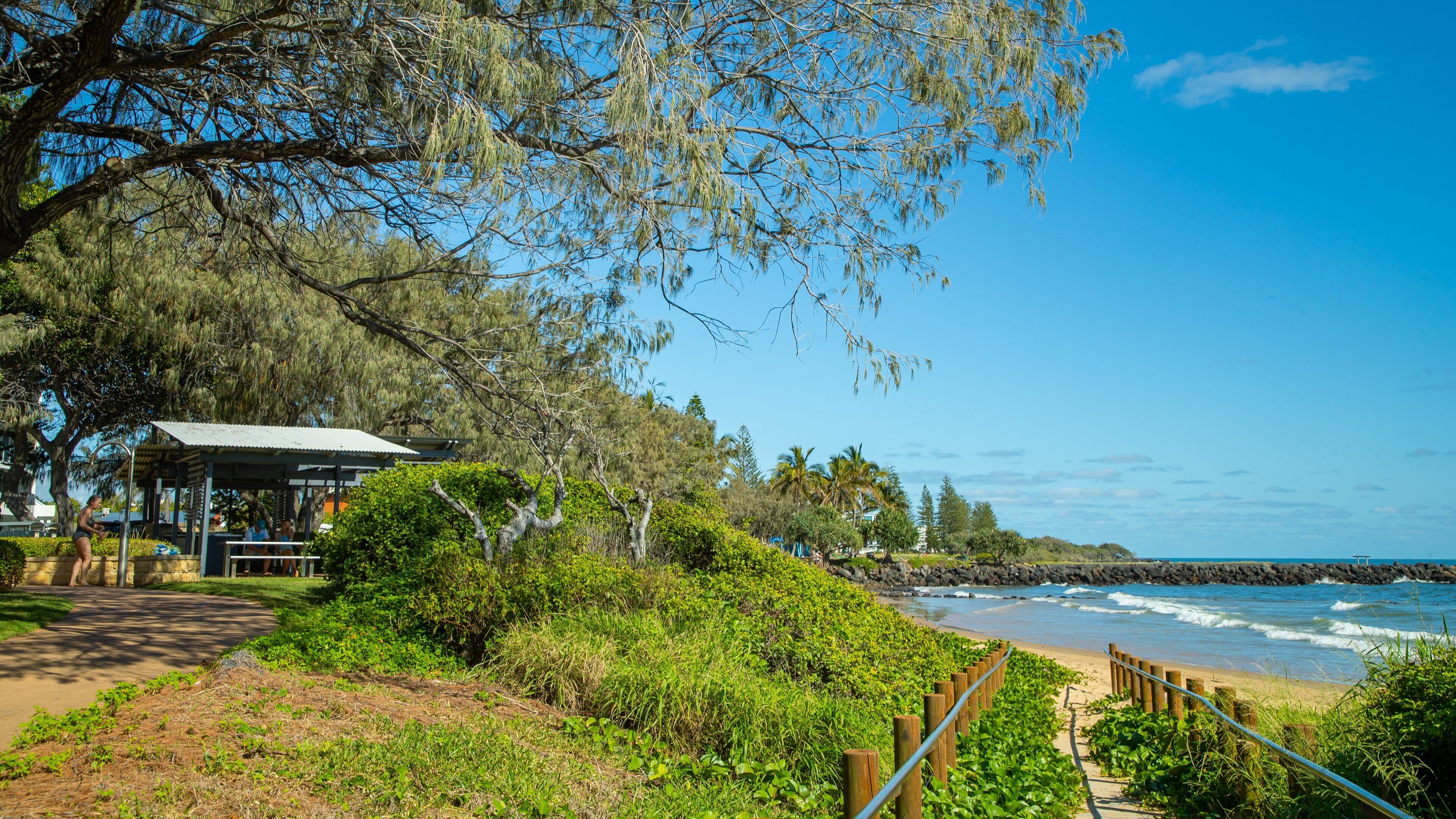 Paisaje costero con playa, costa rocosa y un pabellón cubierto.