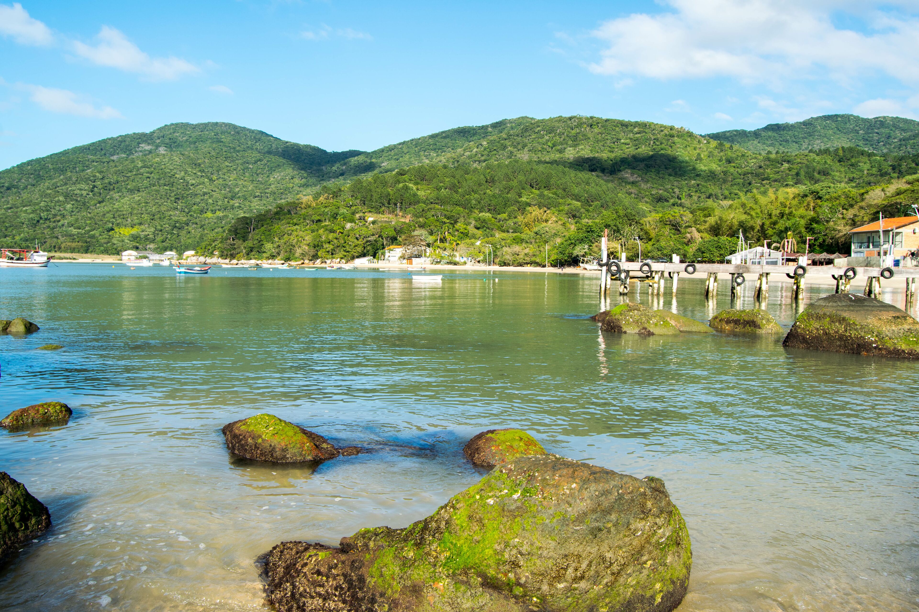 A coastal scene with clear water, rocks, boats, and a mountainous backdrop.