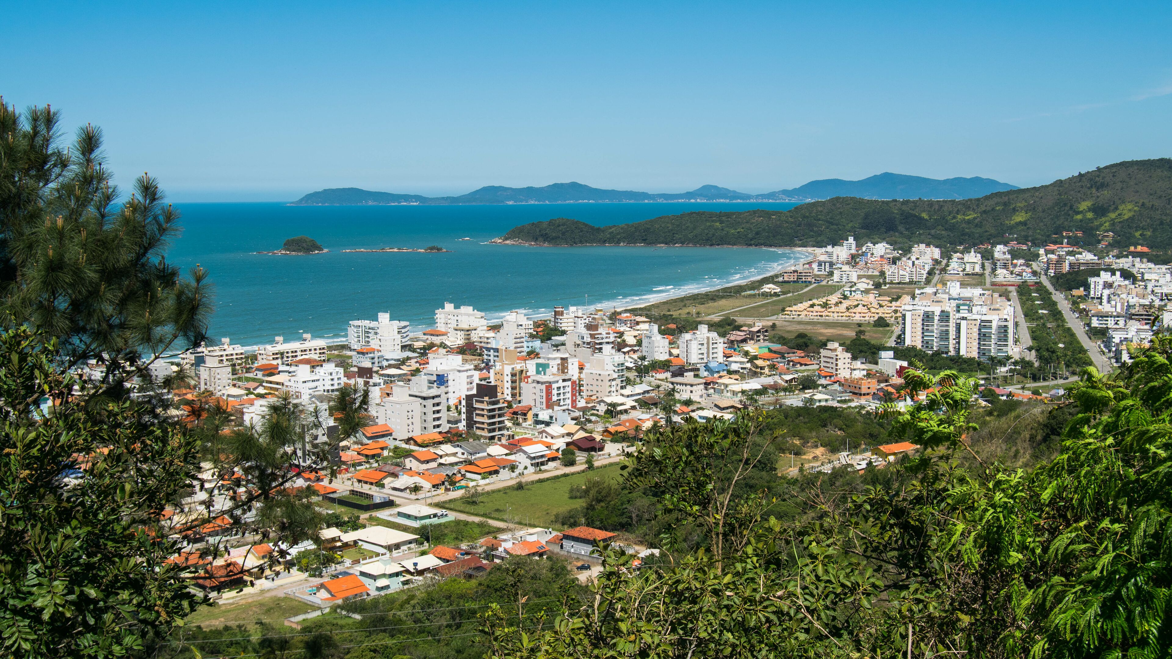 A coastal cityscape with dense urban development, a beach, and distant mountains.