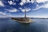 A lighthouse on a small island with the inscription "VOS ET PSAMCI BENEDICENI" in the background.