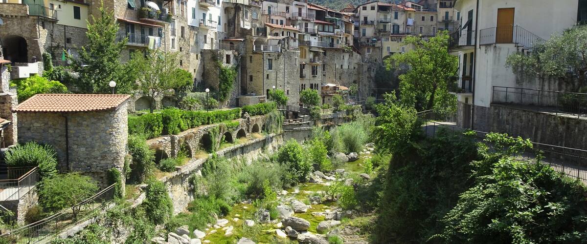 A historic town with stone buildings, a clear stream, and a mountainous backdrop.