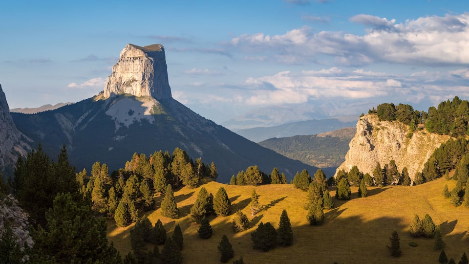 Un paisaje montañoso con una formación rocosa destacada y un bosque denso.