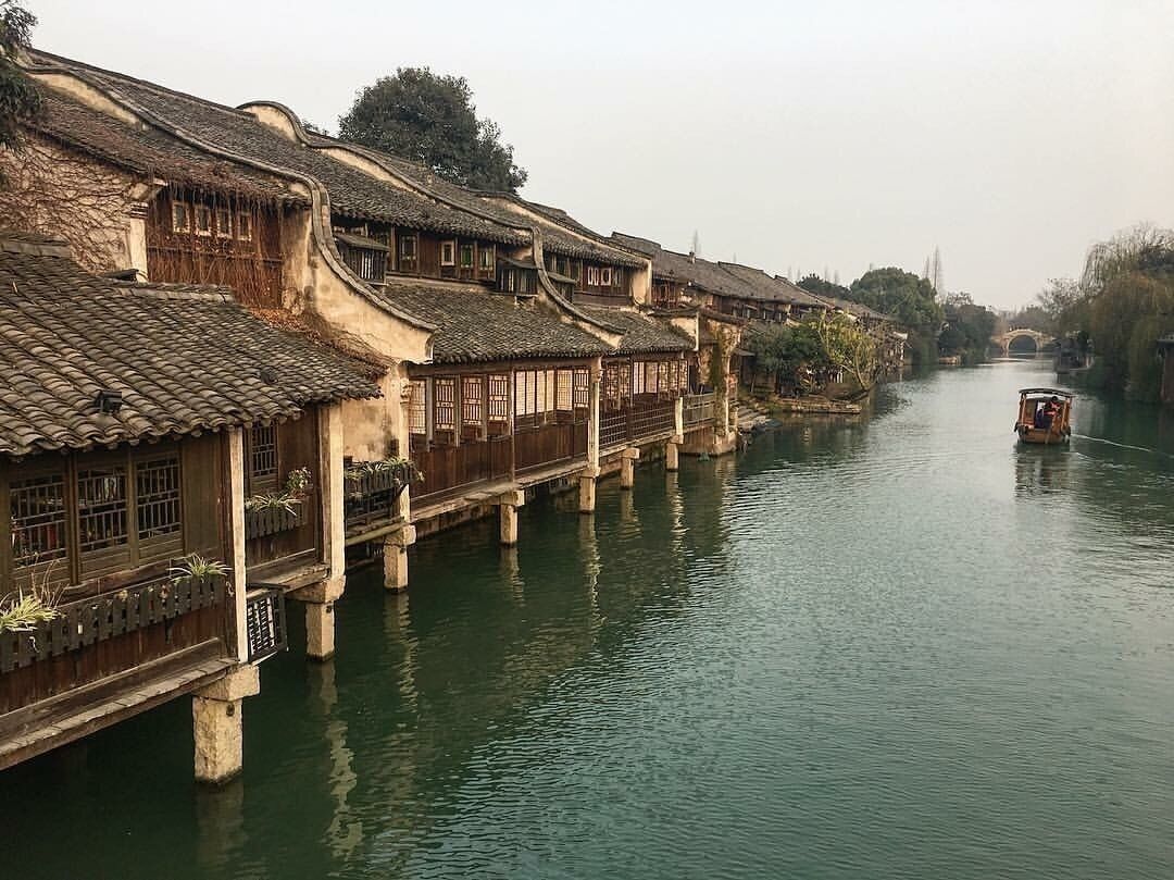 A traditional Chinese water town with wooden buildings and a boat on the river.