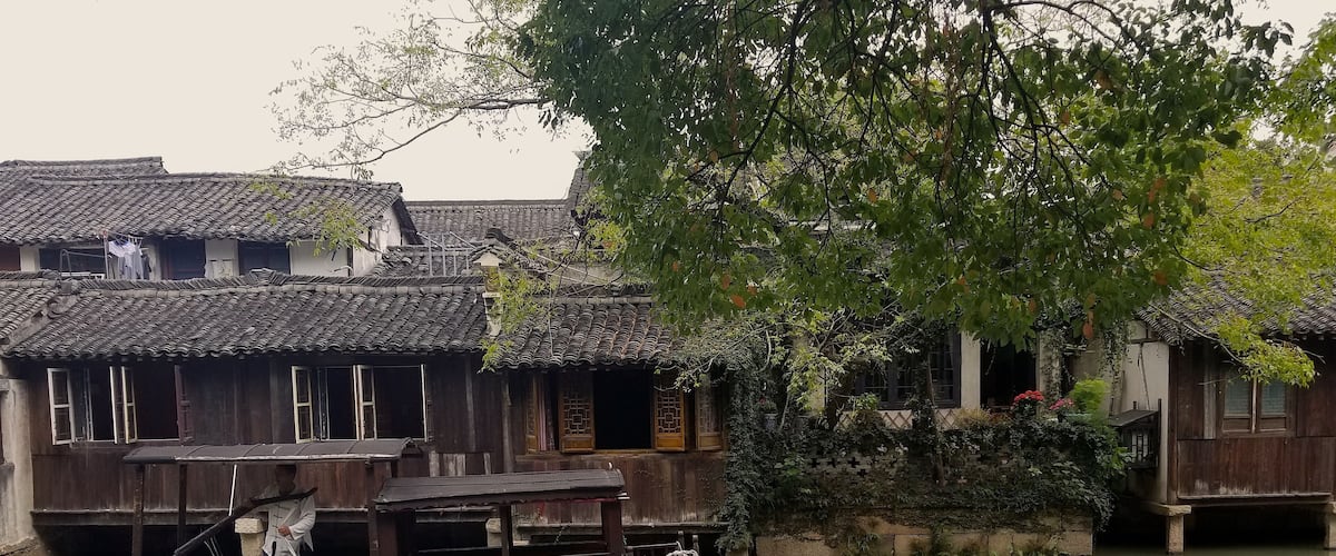 A traditional wooden boat docked near a riverbank with old-style buildings and lush greenery.