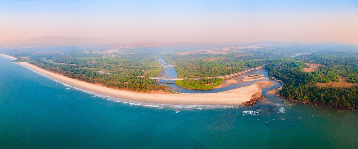An aerial view of a coastal landscape with a beach, a river, and a bridge.