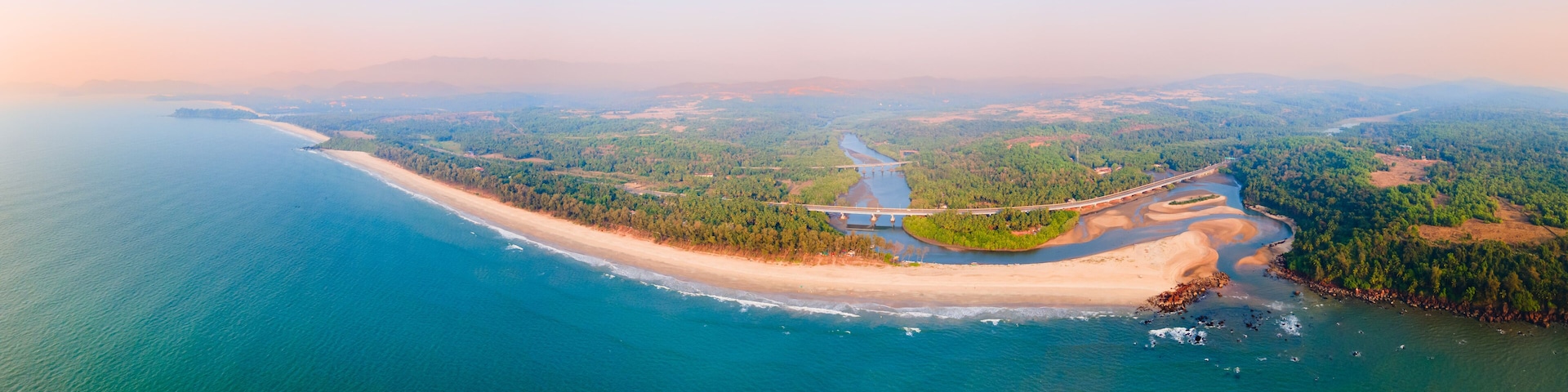 An aerial view of a coastal landscape with a beach, a river, and a bridge.