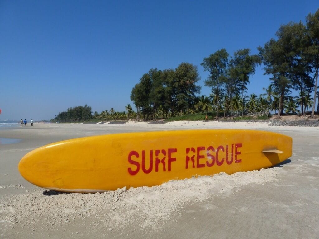 A yellow surf rescue buoy on a sandy beach with palm trees in the background.