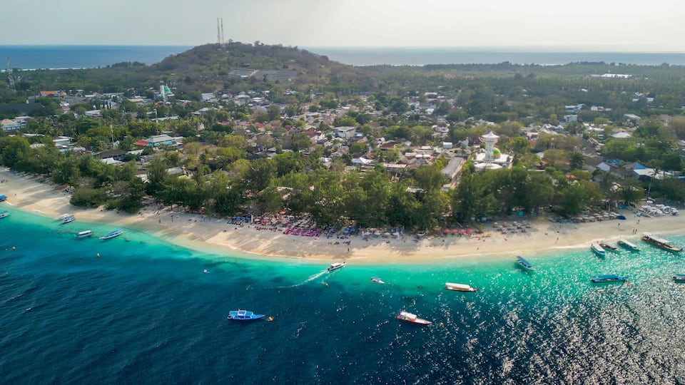 A coastal town with a beach, boats, and a hill with a tower in the background.