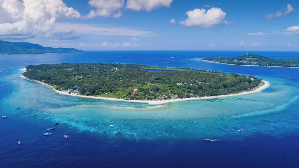An aerial view of a tropical island with clear turquoise waters, a sandy beach, and lush greenery.