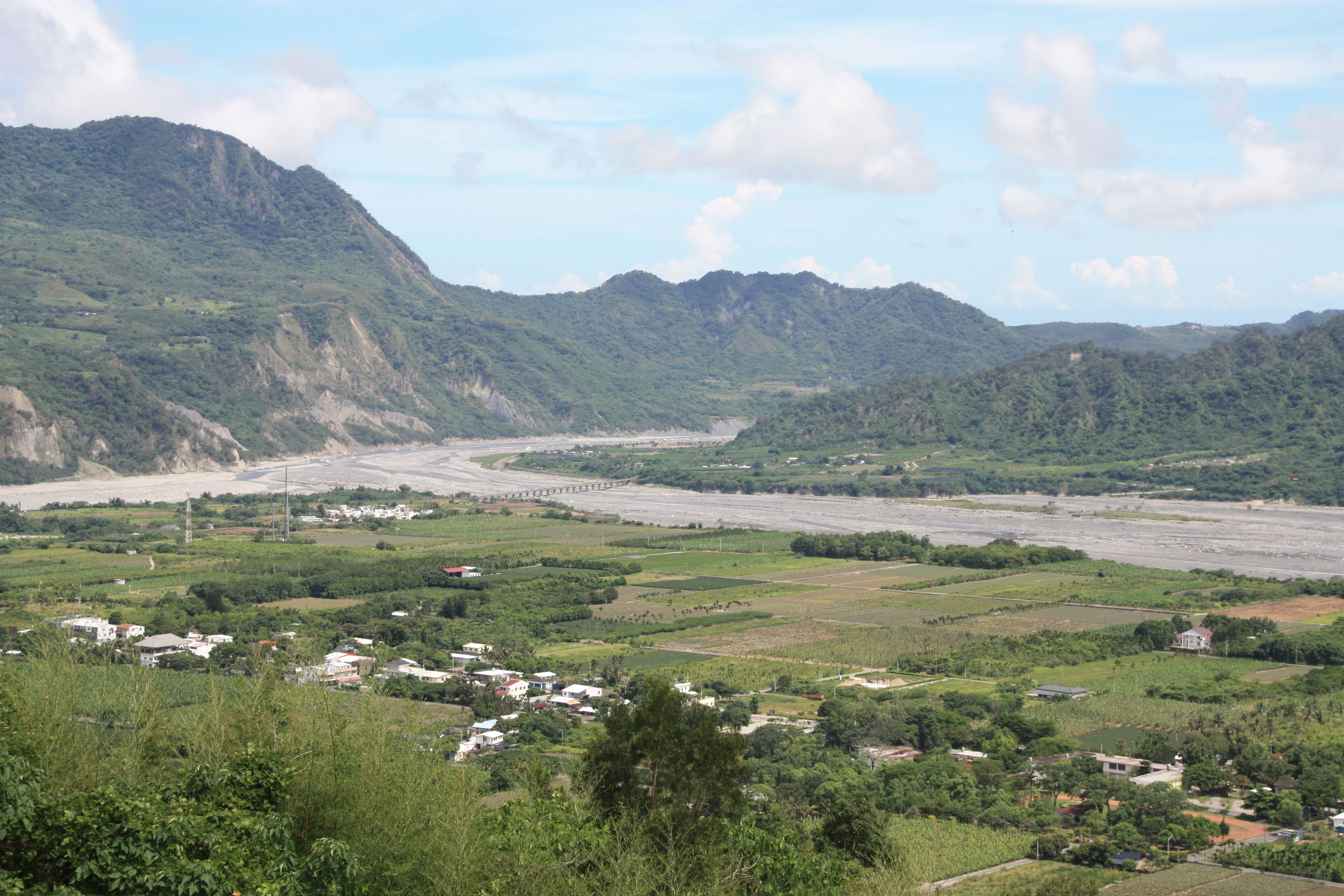 A river valley with mountains, a bridge, and scattered houses.