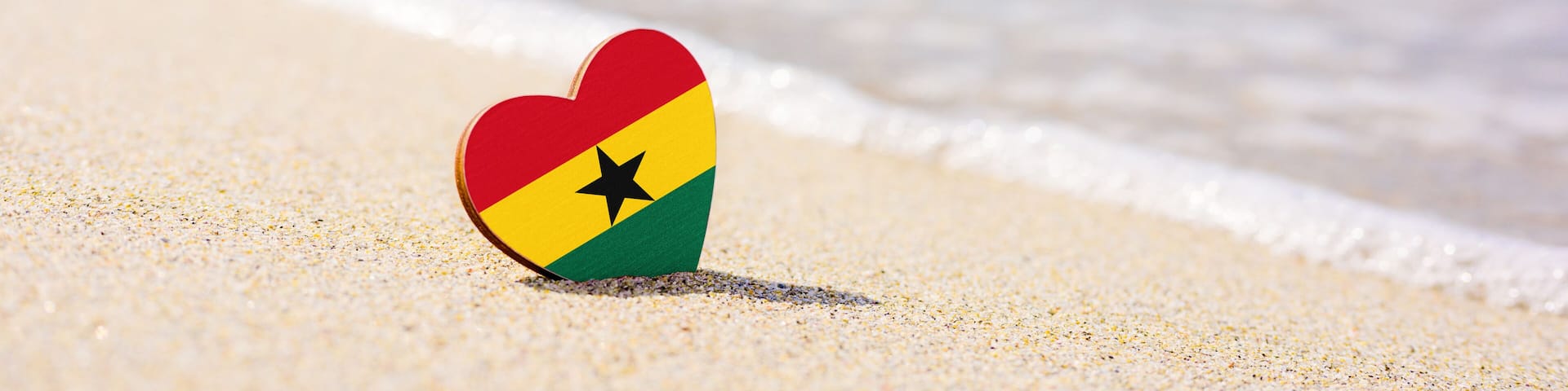 Flag of Ghana in the shape of a heart on a sandy beach. The concept of the best vacation in Ghana