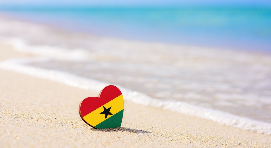 Flag of Ghana in the shape of a heart on a sandy beach. The concept of the best vacation in Ghana