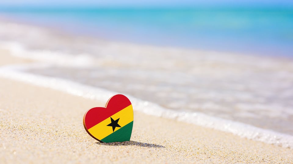 A heart-shaped object with a flag design on a sandy beach with ocean waves.