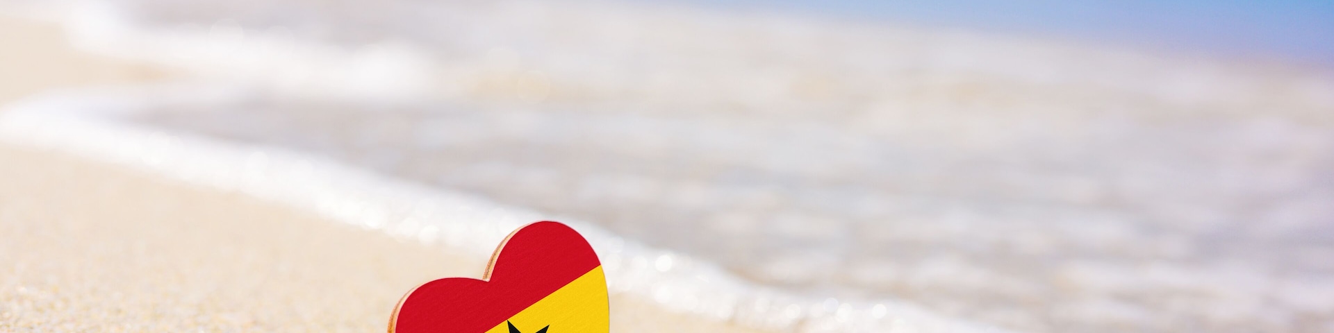 Flag of Ghana in the shape of a heart on a sandy beach. The concept of the best vacation in Ghana