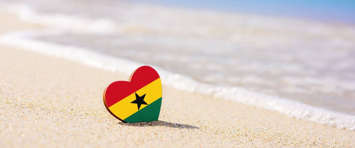 A heart-shaped object with a flag design on a sandy beach with ocean waves.
