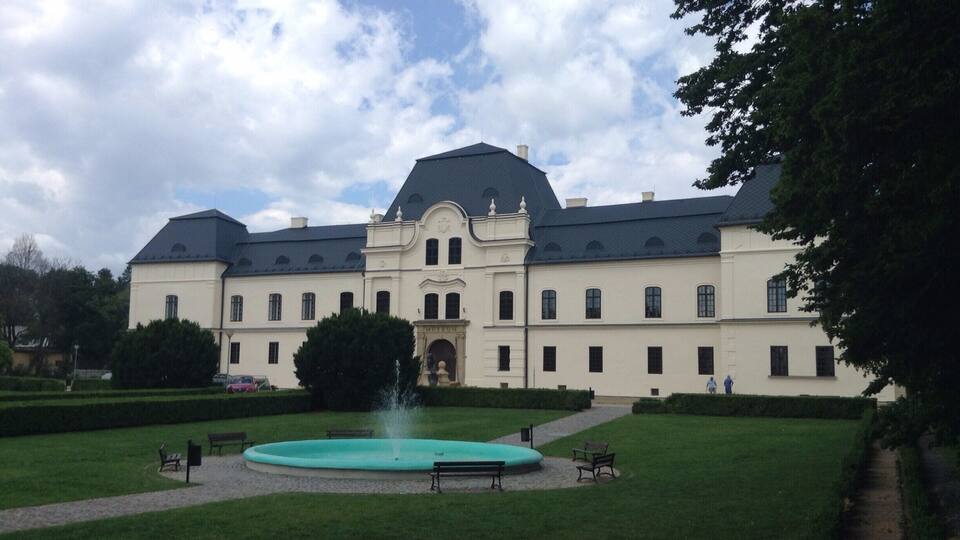 A large, historic building with a central courtyard, a fountain, and a formal garden.