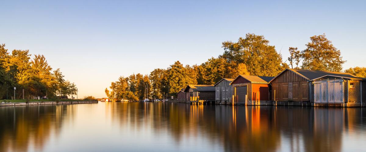 A calm lake with wooden docks and boats, surrounded by trees and clear skies.