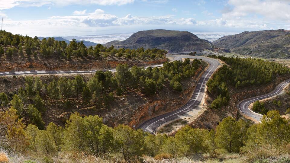 A winding mountain road surrounded by dense forests and rocky terrain.