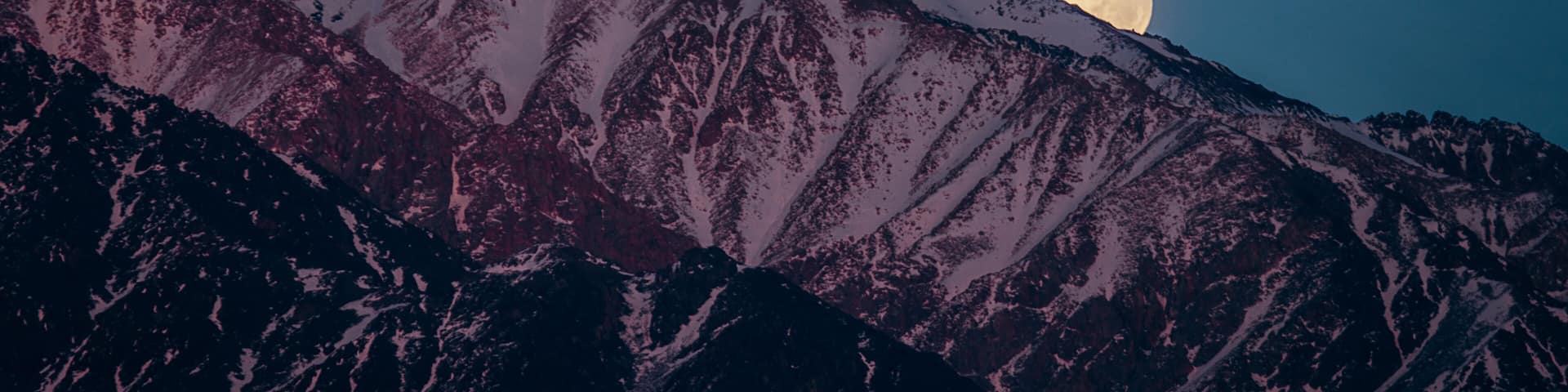 A mountain range with a full moon in the sky.