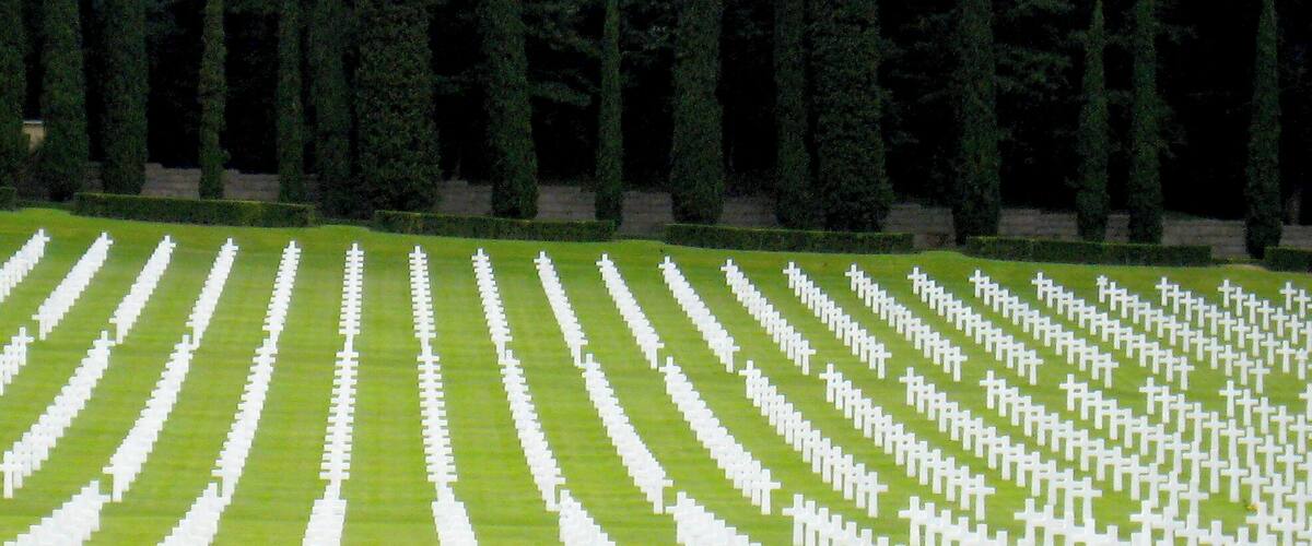 A cemetery with rows of white crosses on green grass.