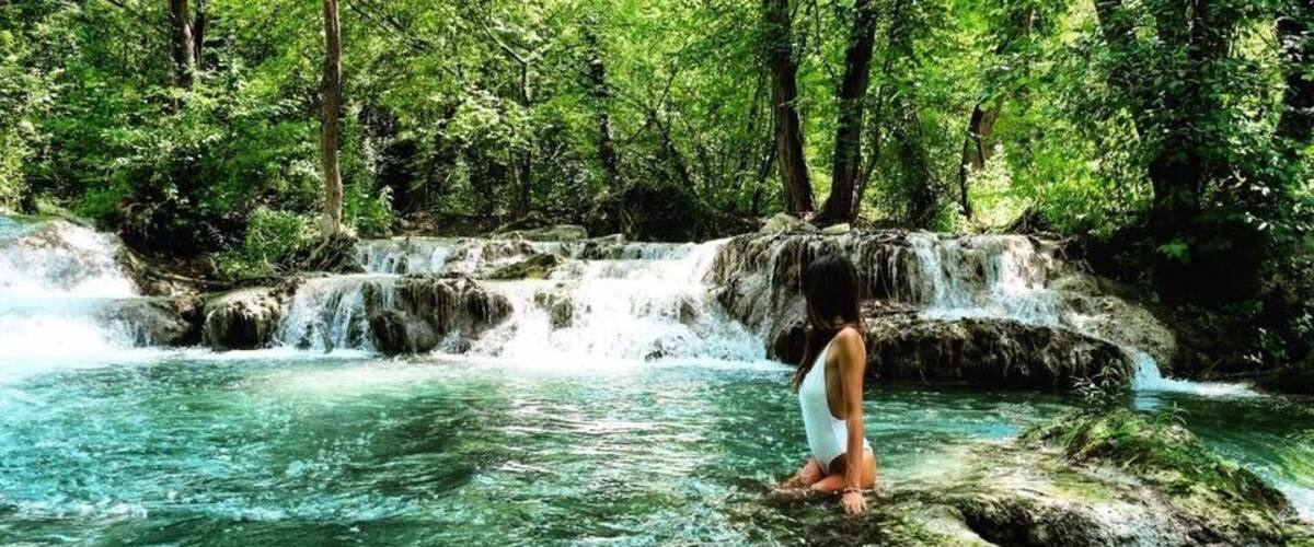 A waterfall in a forested area with clear water and a person standing on rocks.