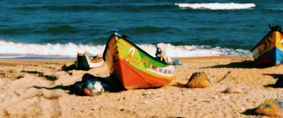 Two colorful boats on a sandy beach with the ocean in the background.