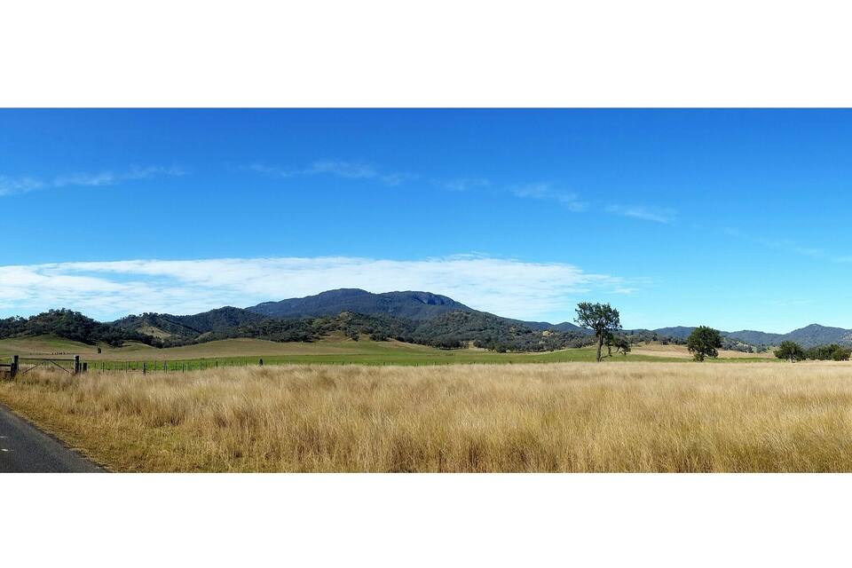 Un campo cubierto de hierba con una valla, un cielo azul despejado y montañas a lo lejos.