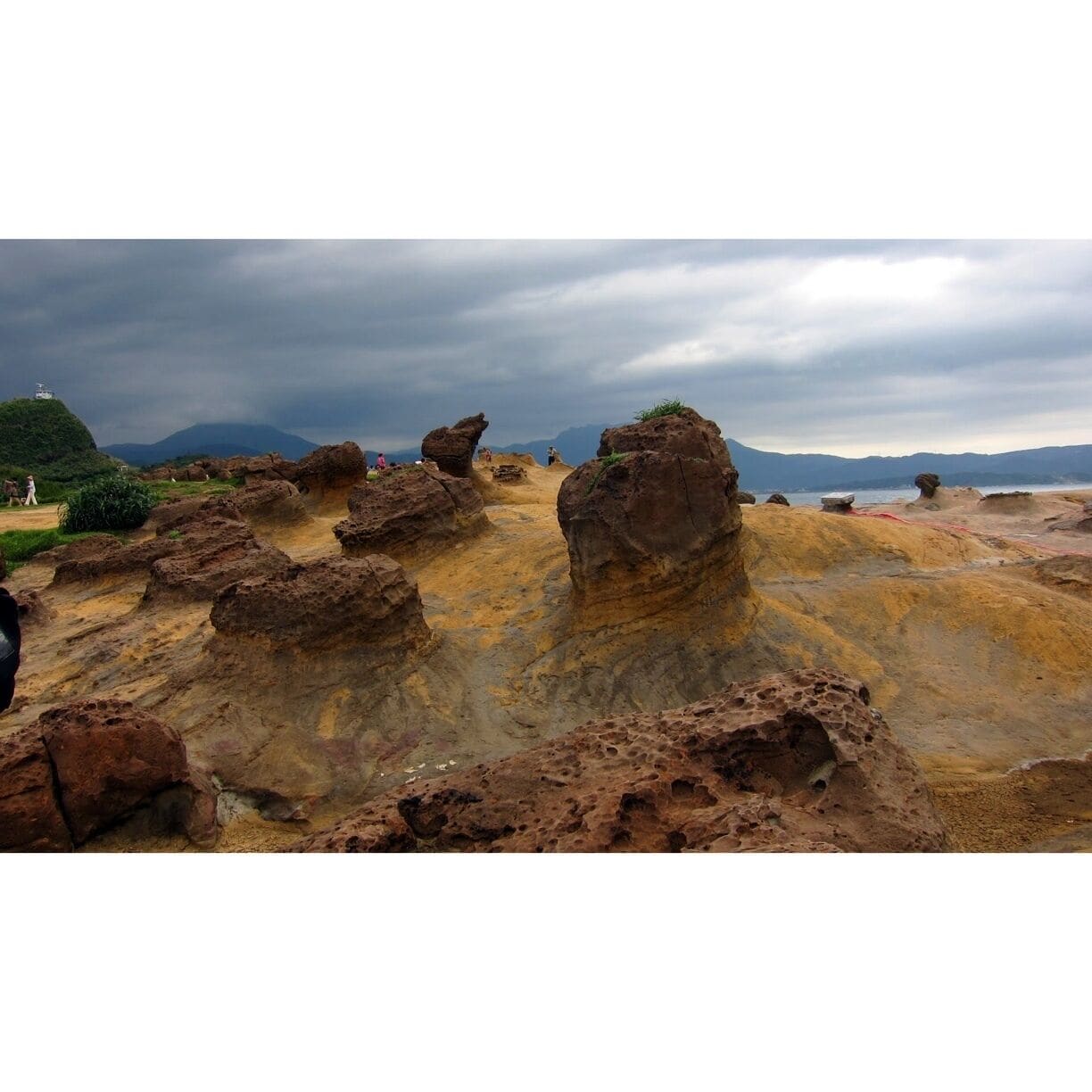 Paisagem rochosa com formações rochosas distintas e uma cordilheira distante sob um céu nublado.