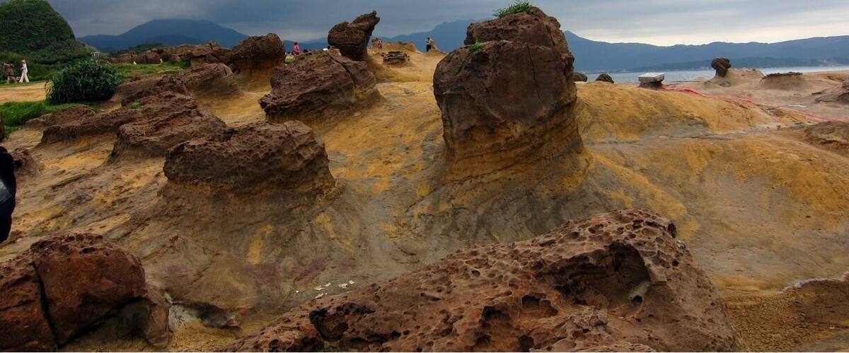 A rocky landscape with prominent rock formations and a distant mountain range under a cloudy sky.