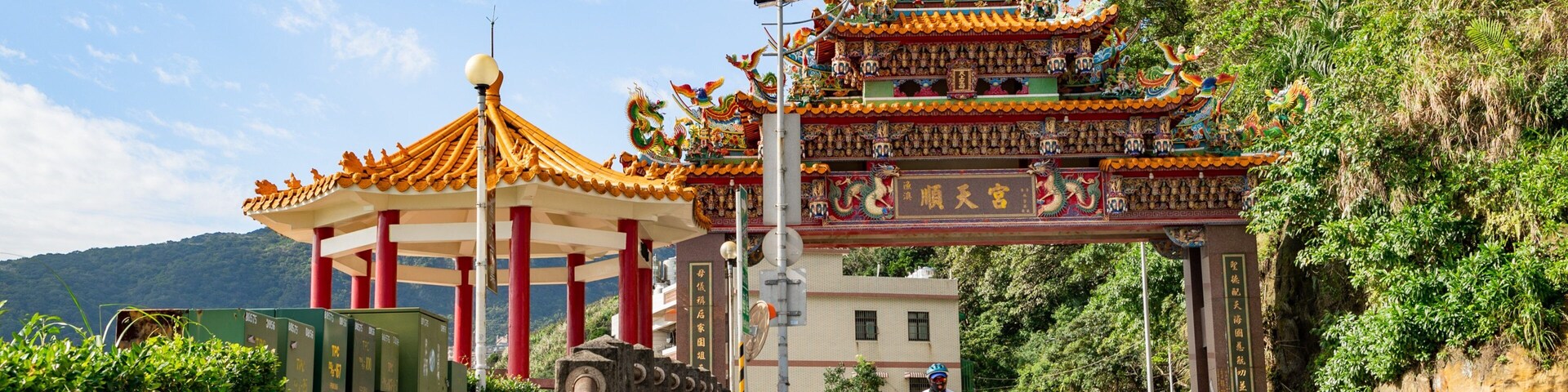 A traditional Chinese gate with intricate dragon decorations, a pagoda, and lush greenery.