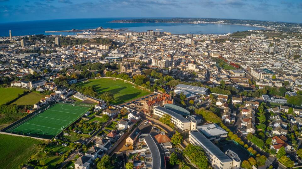 An aerial view of a coastal city with a large stadium, historic buildings, and a marina.