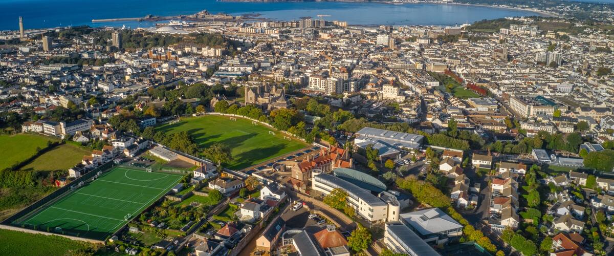An aerial view of a coastal city with a large stadium, historic buildings, and a marina.