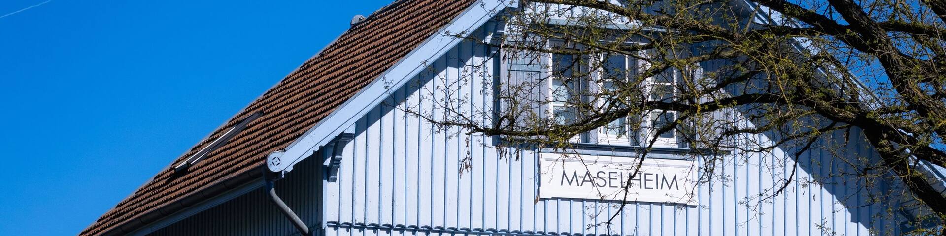 A two-story building with a blue facade and a red-tiled roof, labeled 'MASSEHEIM.'