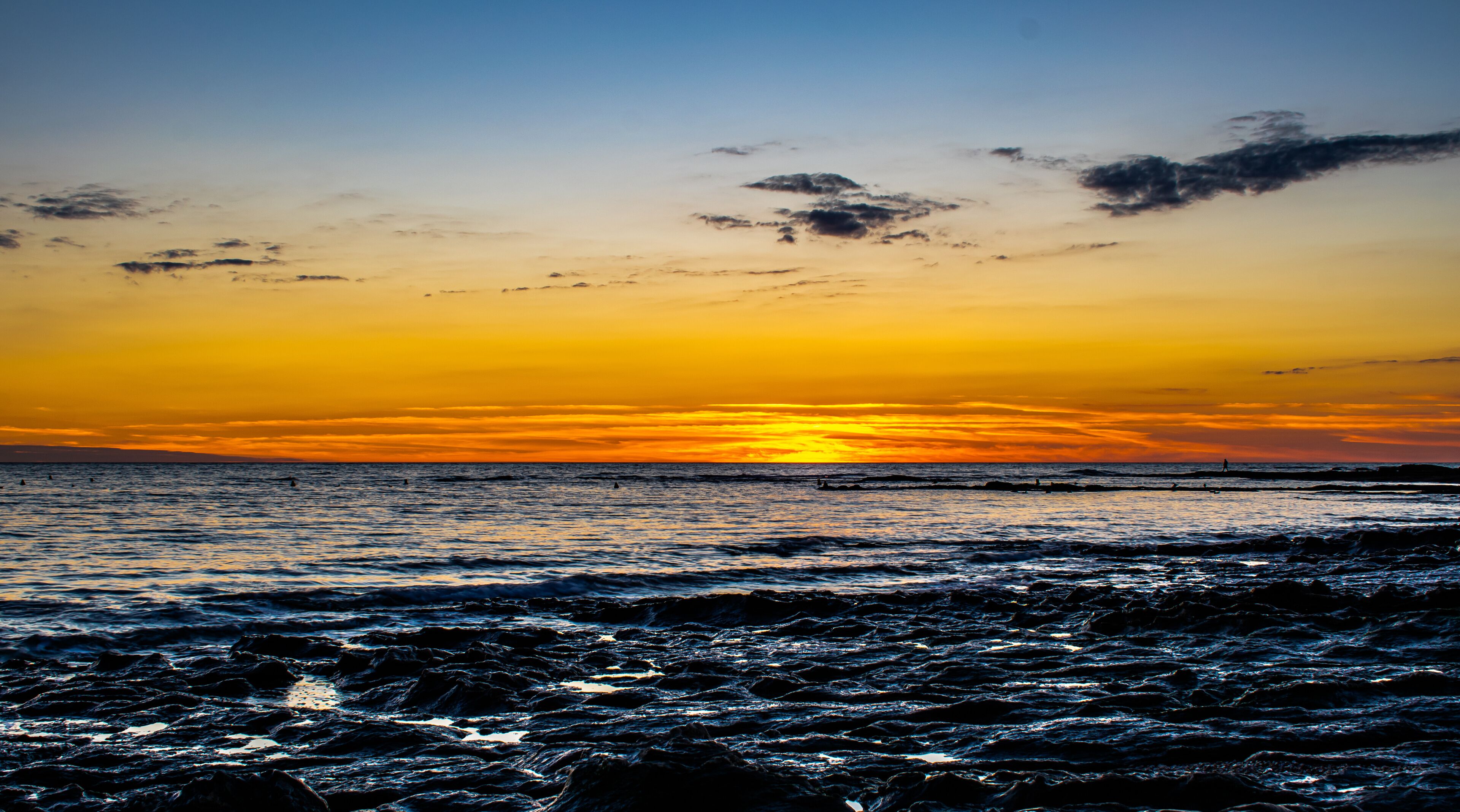 A sunset over a rocky shoreline with waves crashing onto the rocks.