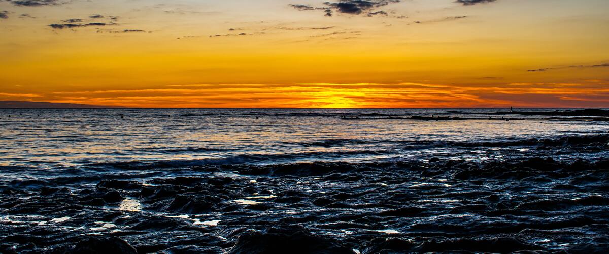 A sunset over a rocky shoreline with waves crashing onto the rocks.