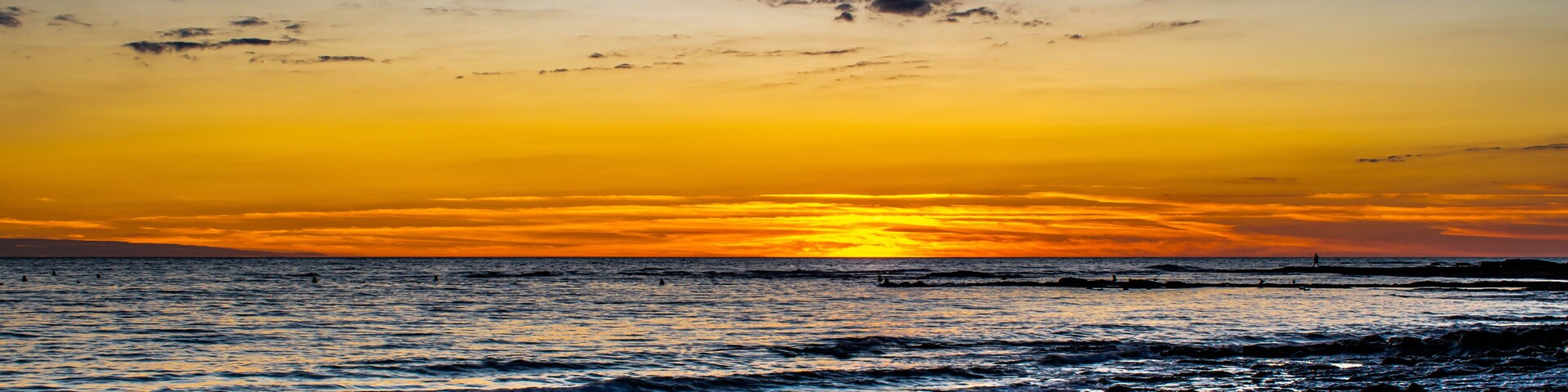 A sunset over a rocky shoreline with waves crashing onto the rocks.
