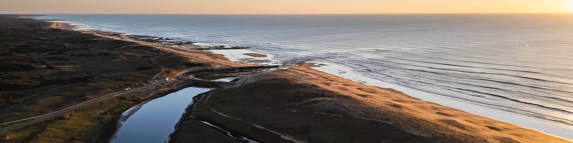 A coastal landscape with a river, sandy beach, and a road.