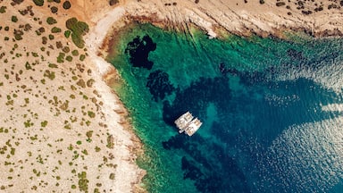 A coastal area with clear turquoise waters, a sandy beach, and a boat anchored near the shore.