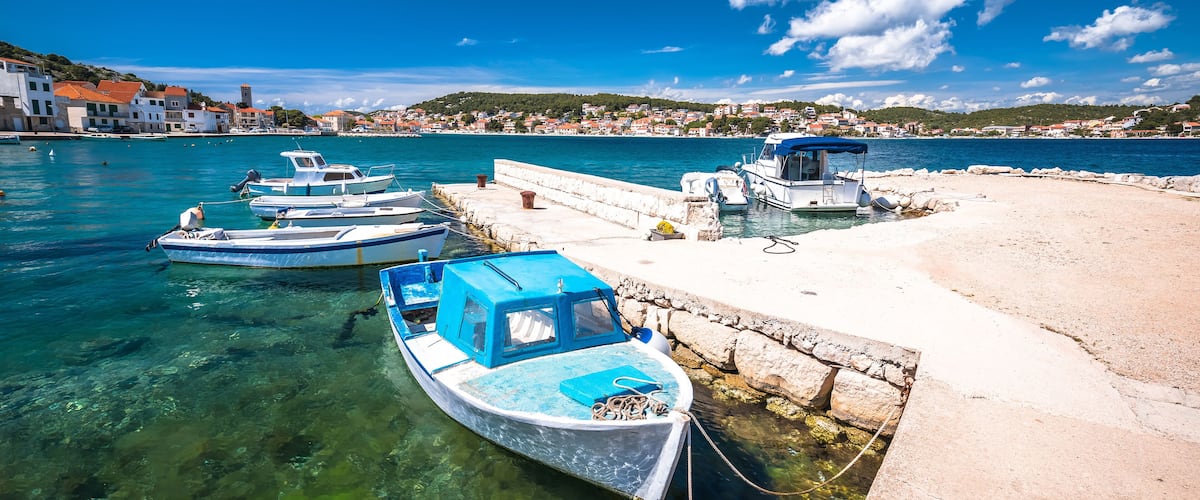 A harbor with boats docked, clear water, and a stone pier.