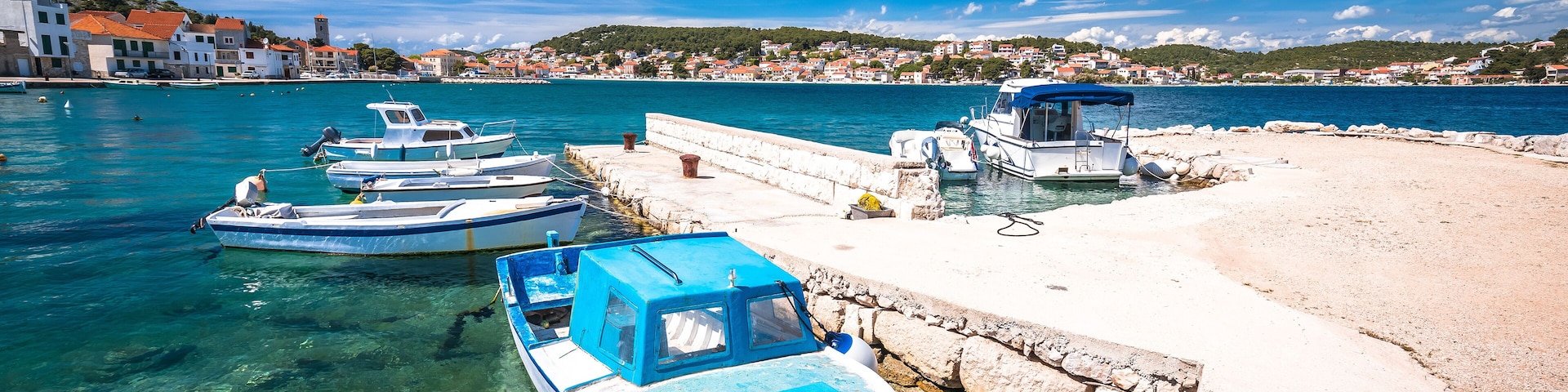 A harbor with boats docked, clear water, and a stone pier.