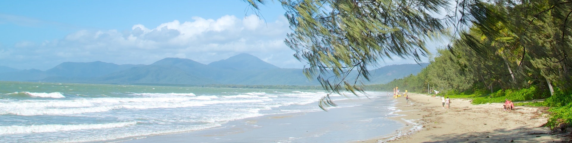 A beach with waves, a clear sky, and mountains in the distance.