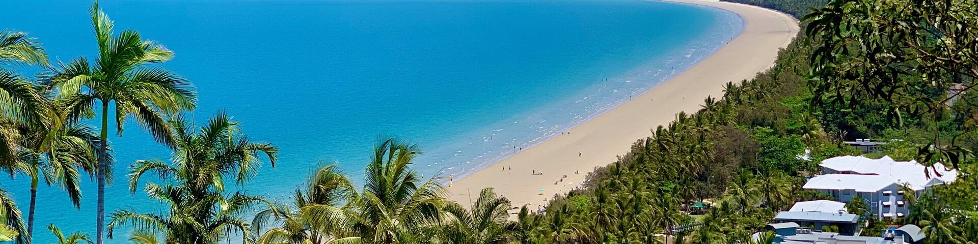 A coastal landscape with a clear blue sea, a sandy beach, and lush green hills in the background.
