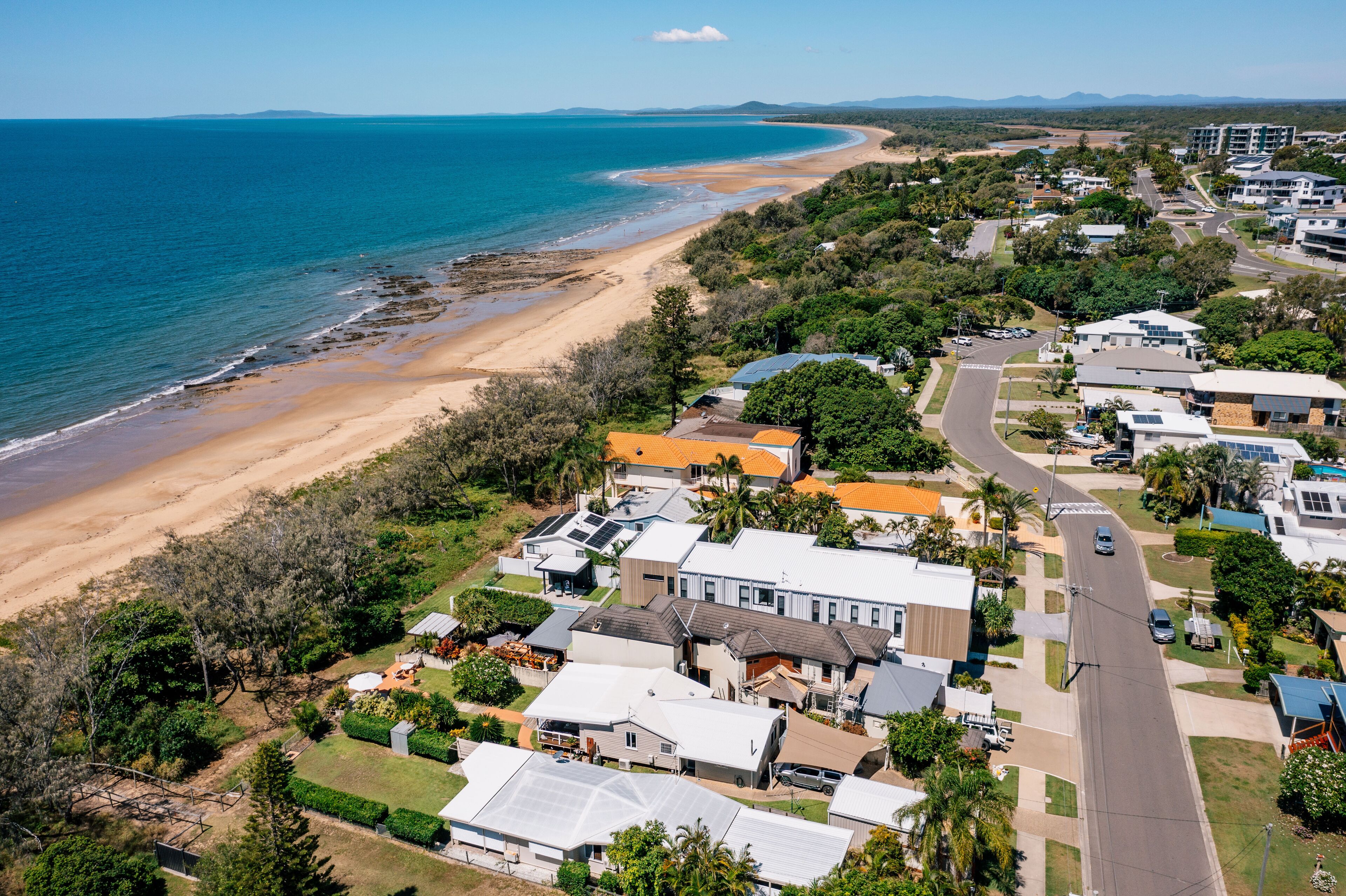 A coastal residential area with houses, a beach, and a clear blue sky.
