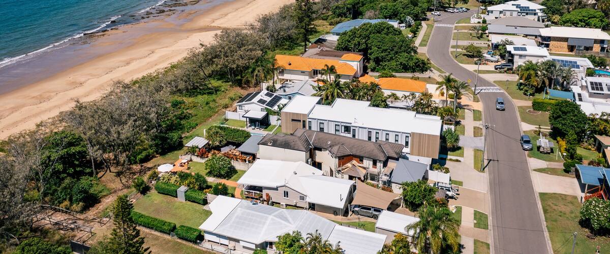 A coastal residential area with houses, a beach, and a clear blue sky.