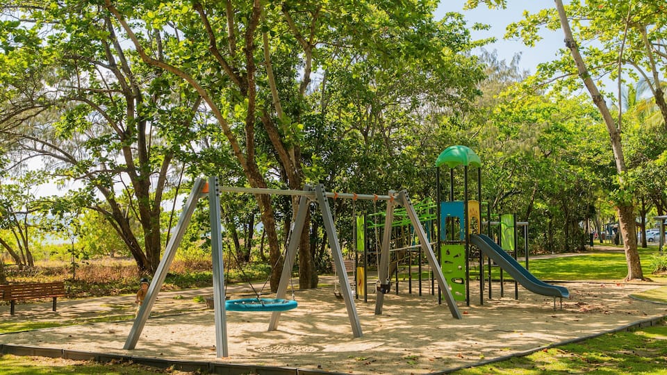 Ein Spielplatz mit Schaukeln, Rutschen und einer Kletterkonstruktion, umgeben von Bäumen.