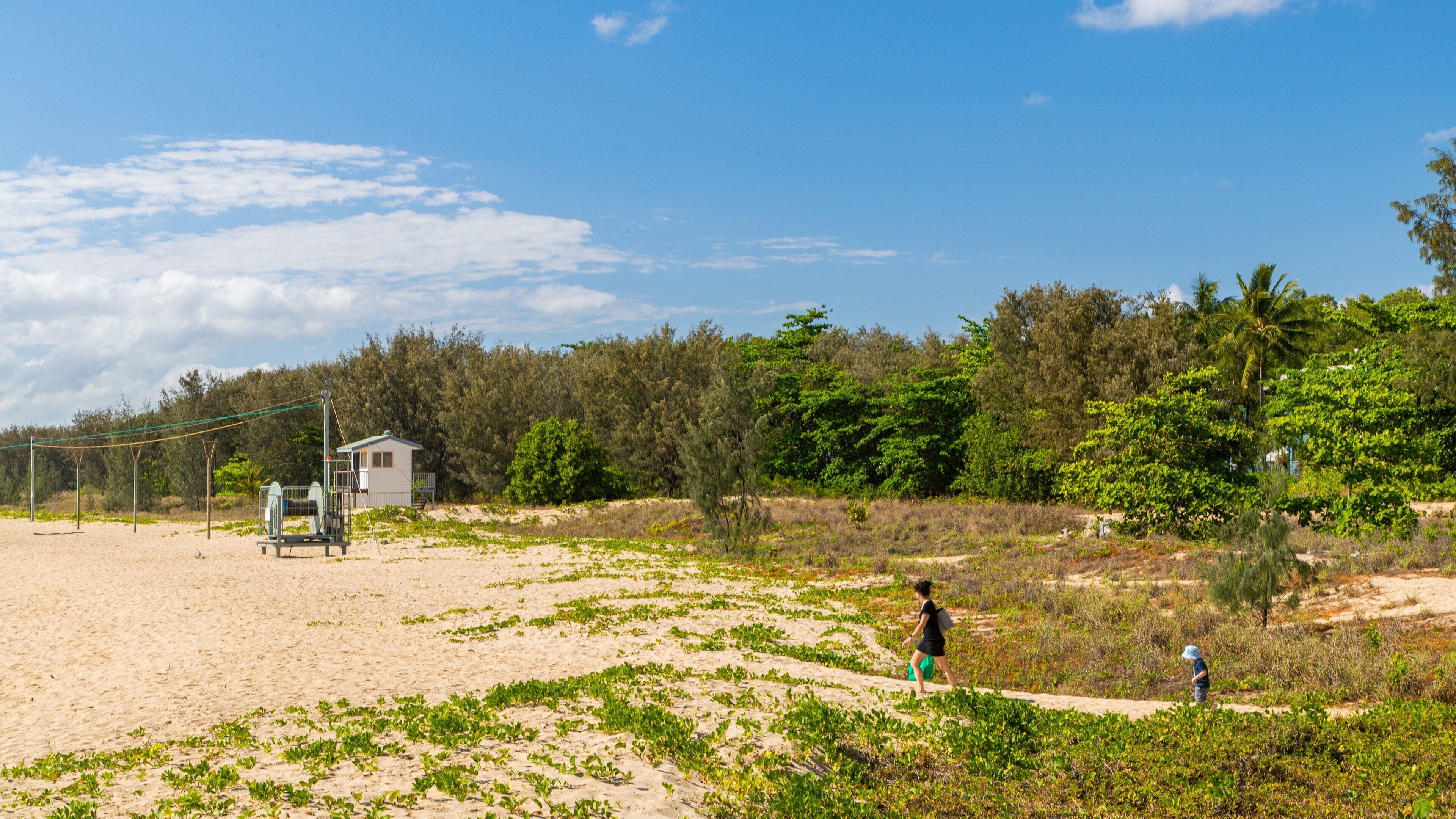 A beach with a lifeguard tower, a sandy path, and dense greenery in the background.